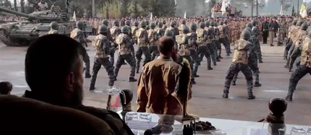 Seated on a podium, Zahran Alloush watches Islam Army fighters and armored vehicles parading through the Eastern Ghouta, 2015. Source: rebel video.